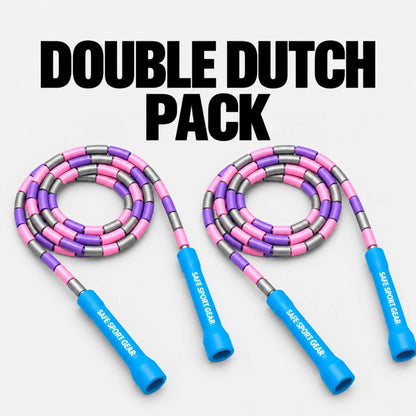 Two pink and purple jump ropes with blue handles and silver metal accents, arranged side by side on a light gray background with the text 'DOUBLE DUTCH PACK' at the top. The handles are branded with 'SAFE SPORT GEAR'.