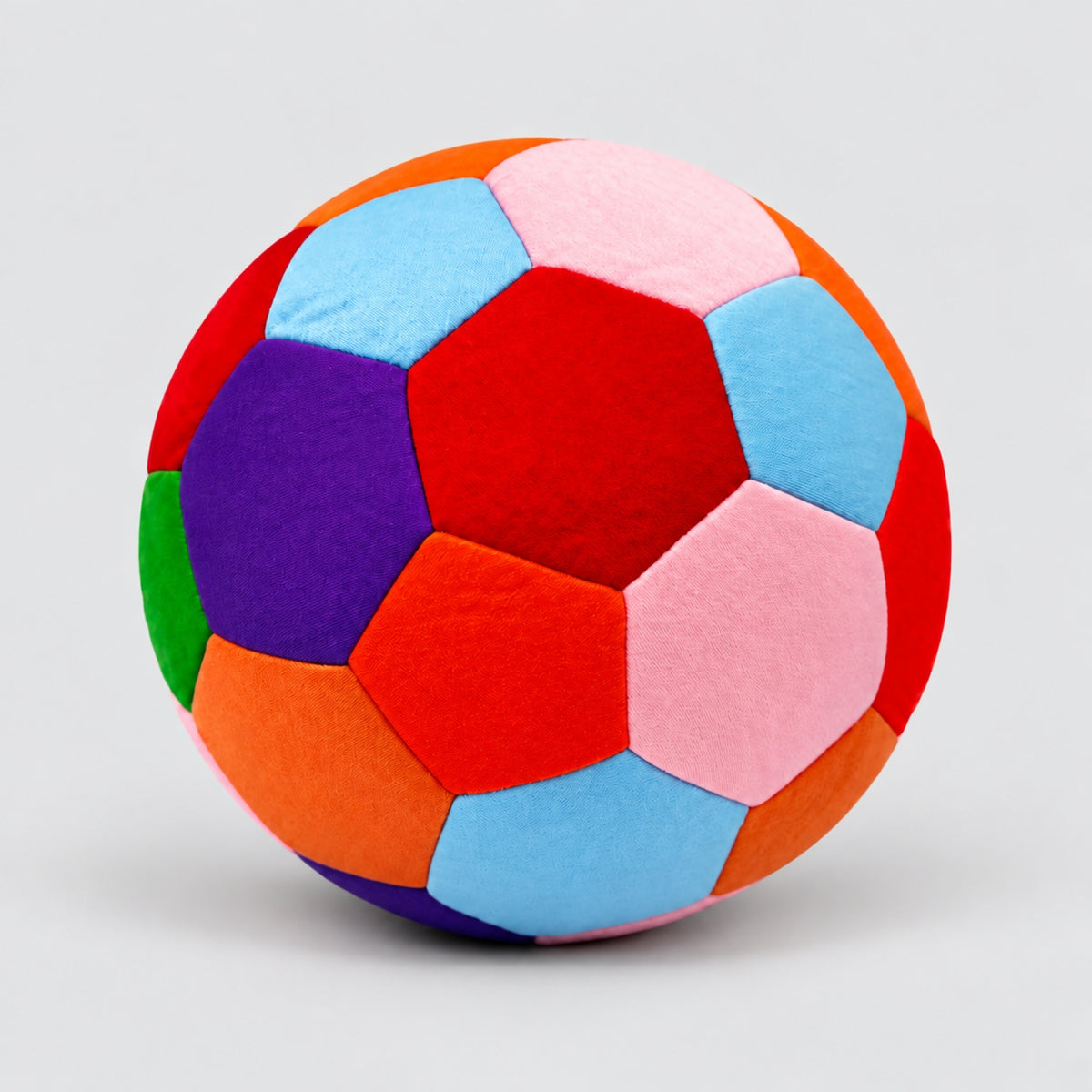 A colorful house ball with stitched hexagonal panels in red, orange, light blue, pink, purple, green, and dark red, photographed on a light gray background.