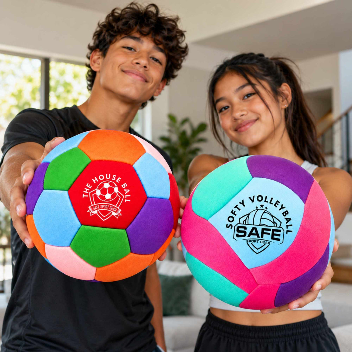 Two children holding colorful house ball and softy volleyball in a bright indoor room. The house ball has multiple bright colors including pink, purple, blue, green, orange, and red, with printed text including 'THE HOUSE BALL' and Safe Sport Gear logo.