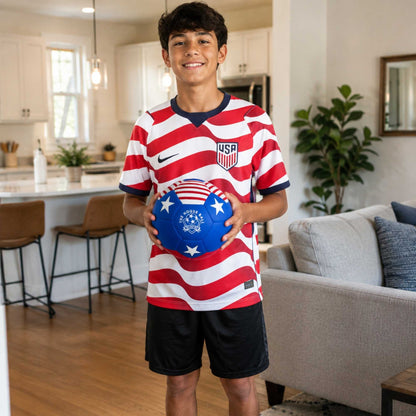 Young boy in a USA-themed sports jersey holding a House Ball - USA with a star design in a living room.