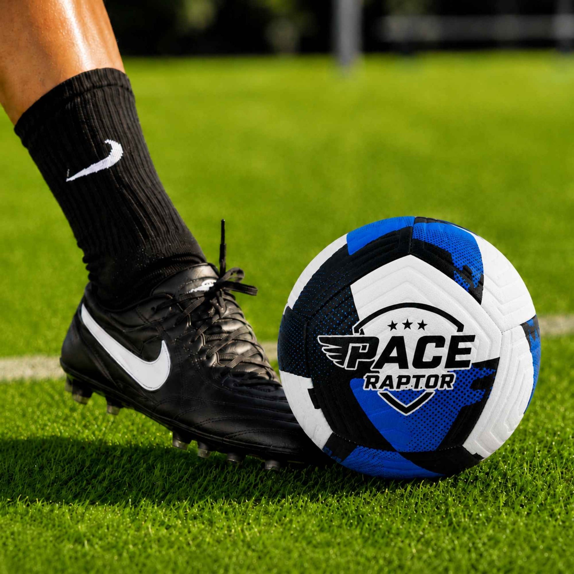 Pace Raptor Size 5 Soccer Ball - Blue on a grass field, close-up of foot and cleats.