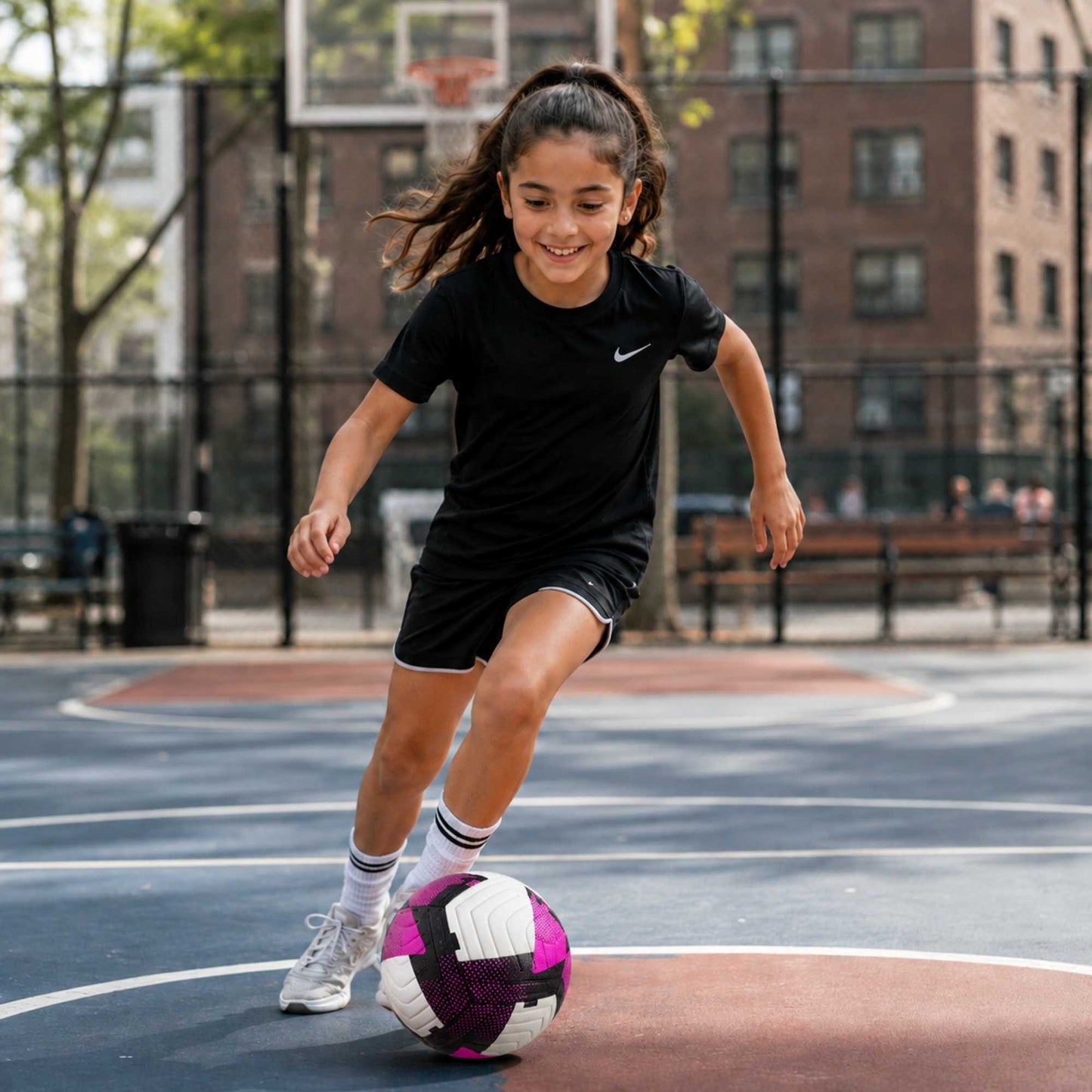 Girl playing with a Pace Raptor Size 4 Soccer Ball - Purple on an outdoor court with a building in the background