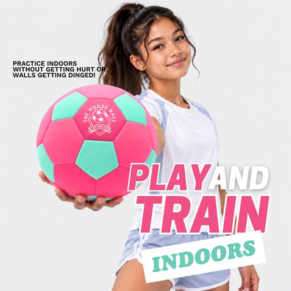 A young girl in a white athletic jersey holds a pink and mint green indoor soccer ball against a light gray background, with promotional text overlays reading 'PRACTICE INDOORS WITHOUT GETTING HURT OR WALLS GETTING DINGED!' and 'PLAY AND TRAIN indoors'.