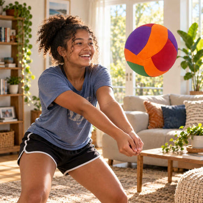 A woman in a blue t-shirt and black athletic shorts smiles while reaching for a colorful softy volleyball floating in a bright, modern living room.