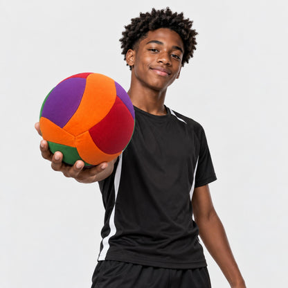 A young man holding a colorful, multi-panel softy volleyball in his hand, wearing a black athletic t-shirt with white side stripes and black shorts, against a light gray background.
