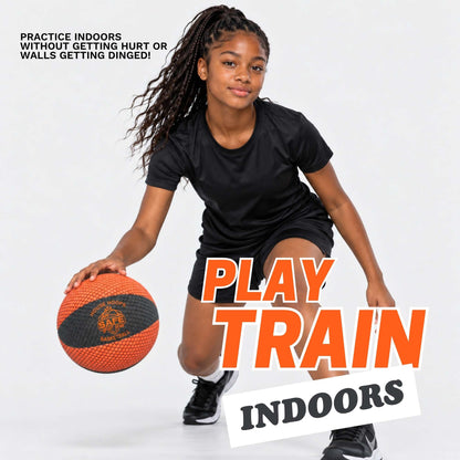A young girl with long dark braids is crouching indoors while dribbling a black and orange indoor basketball. She is wearing a black athletic T-shirt and black shorts.