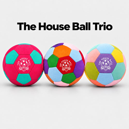 Three colorful indoor soccer balls displayed side by side on a light gray background with the text 'The House Ball Trio' above them. The balls feature multiple bright colors in a geometric pattern, with a purple, pink, green, and orange center panel printed with the 'Safe Sport Gear' logo.